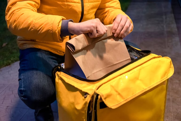 repartidor-chaqueta-amarilla-abriendo-mochila-amarilla-tomando-bolsa-orden